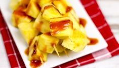 pineapple skewers with ketchup on a white plate next to a red and white checkered napkin