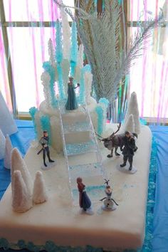 an ice castle cake with figurines on top and frosted trees in the background