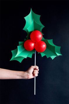 a hand holding an umbrella made out of paper with holly leaves on it and two cherries