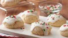 small cookies with icing and sprinkles on a white tray next to a glass bowl