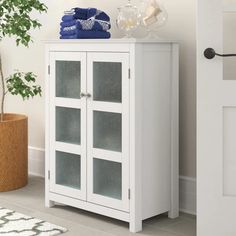 a white cabinet sitting next to a potted plant and glass door with towels on top