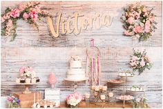 a table with cakes and desserts on it that are decorated with pink flowers in front of a wooden wall