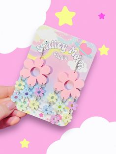 a pair of pink flower shaped earrings on top of a card with stars and clouds in the background