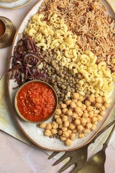 a white plate topped with pasta and beans next to a bowl of sauce on top of a table