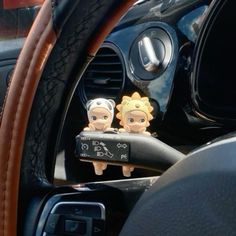 two little figurines sitting in the center console of a car, next to a steering wheel