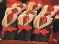 hotdogs wrapped in paper with red bows are sitting in a box on a table