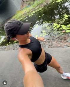 a woman in black shirt and hat riding skateboard next to water with green plants