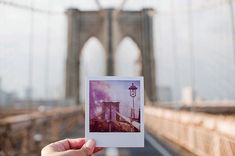 someone holding up a polaroid in front of the brooklyn bridge