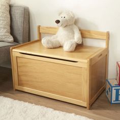 a white teddy bear sitting on top of a wooden toy box next to a couch