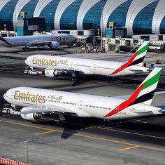 two airplanes are parked on the tarmac in front of an airport terminal with other planes