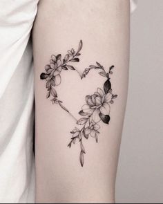 a heart shaped tattoo with flowers and leaves on the side of the arm is shown