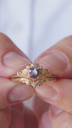 a person holding a gold ring with a purple stone in it's center and diamond accents around the band