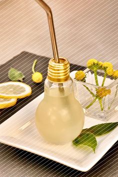 a light bulb shaped vase with flowers in it on a plate next to lemons