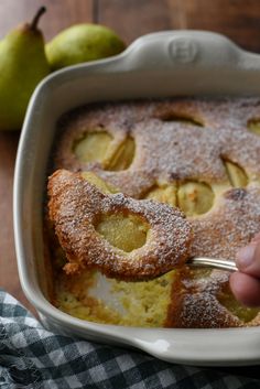 a person is spooning some food out of a casserole dish with apples in the background