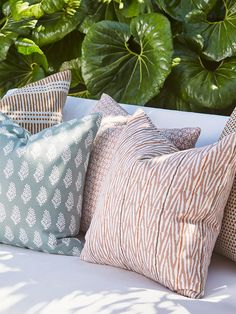 four pillows on a white couch in front of green plants