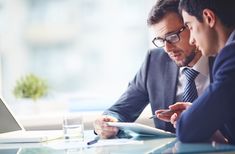 two men in suits are looking at something on a tablet