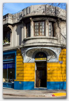 a yellow and blue building on the corner of a street in front of a tree