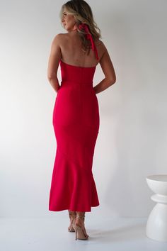 a woman in a red dress is standing with her back turned to the camera and looking down