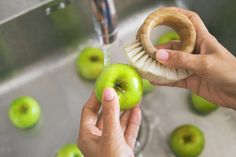 a person is washing an apple in a sink with a brush and toothpaste