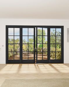 an empty room with black doors and windows looking out onto the trees outside in the day time