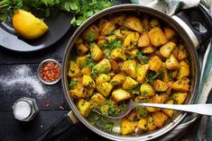 a pan filled with potatoes and parsley on top of a table next to lemons