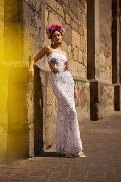 a woman in a white dress leaning against a stone wall with flowers on her head