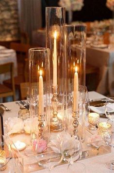 there are many candles that are in the glass vases on the table with flowers