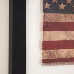 an american flag hanging on the wall next to a black framed photograph with white trim