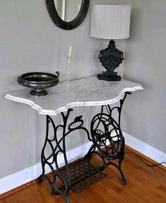 an antique sewing machine table with a mirror on the wall above it and a lamp next to it