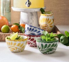 four bowls filled with fruit and vegetables on top of a white tablecloth next to a cake stand