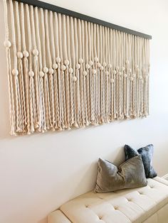 a white bench sitting in front of a wall hanging with macrame balls and tassels