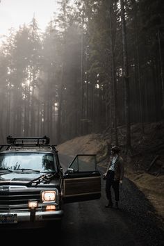 a man standing next to a truck on the side of a road in front of trees