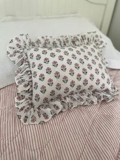 a white bed topped with pillows and a red striped comforter on top of it