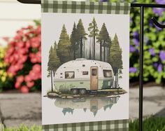 an rv is parked in the grass near some flowers and trees on a flag pole