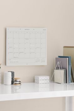 a white desk topped with lots of office supplies and a calendar on top of it