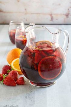 a pitcher filled with liquid next to sliced oranges and strawberries