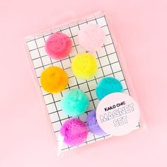 four different colored pom - poms in a package on top of a pink background