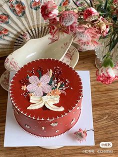 there is a red cake with flowers on it and a fan next to the cake