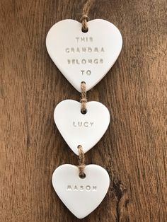 three ceramic heart ornaments hanging from twine on a wooden table with the words, this grandma belongs to lucky mason