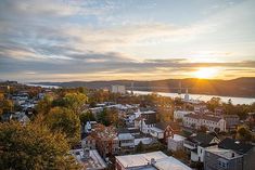 the sun is setting over a city with lots of buildings and trees in front of it