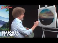 an image of a man painting on the easel in front of a mountain scene