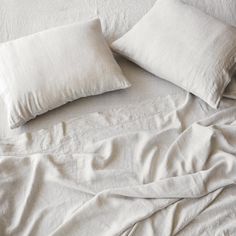 two white pillows on top of a bed with sheets and covers pulled up to the side