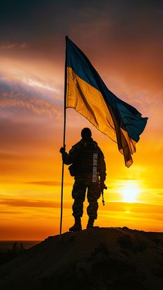 a man holding a flag standing on top of a hill at sun set in the background