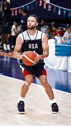 a man holding a basketball on top of a hard wood floor in front of an audience