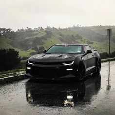 a chevrolet camaro is driving down the road in the rain