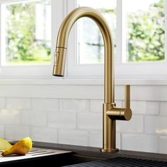 a kitchen sink with a gold faucet and some fruit on the counter top