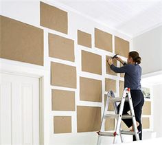 a woman is painting a wall with brown squares on it and she is using a paint roller