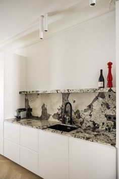 a kitchen with marble counter tops and white cabinets in the corner, along with red vases