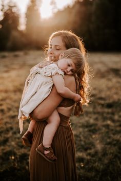 a woman holding a baby in her arms while the sun shines through the trees