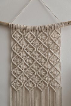 a white wall hanging made with yarn and wood dows on top of a wooden stick